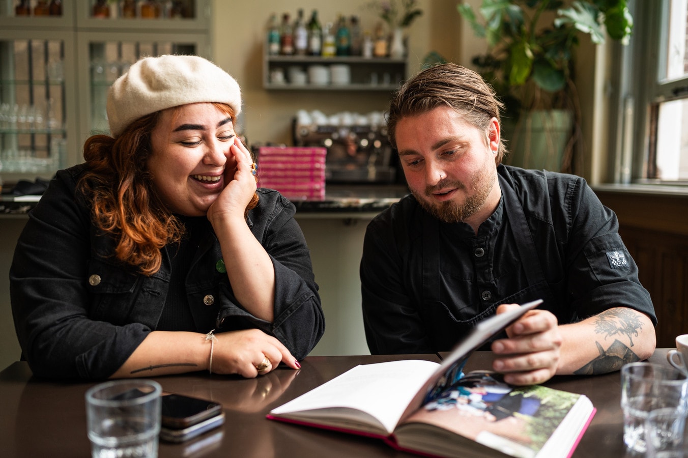Demian Parasmo, chef-kok van Konijnenvoer in Arnhem bekijkt zijn boek ‘The storm we adore’ samen met zijn partner Imane Dafer, mede-eigenaar van Konijnenvoer. Foto: Milan Schellingerhout
