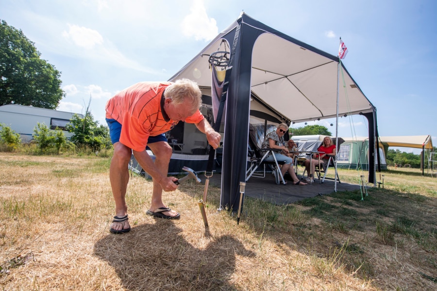Roelof Oving slaat haringen de grond in op camping De Heidebloem in Haarle (Hellendoorn). De dames kijken toe. Foto: Lenneke Lingmont