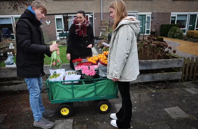 Luke de Jong helpt Rosa Schnater met verkopen van bloemen aan de deur. Foto: AD/Catrinus van der Veen.