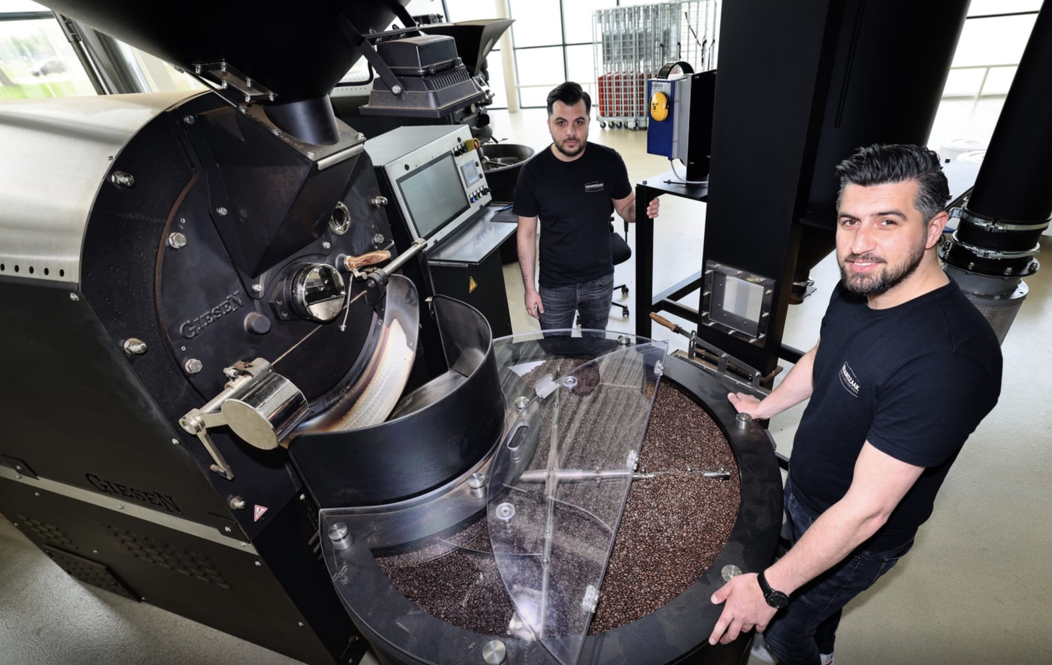 Harun Bingul (rechts) van koffiebranderij Brandzaak in Vierpolders bij de machine waar de bonen gebrand worden, links zijn broer Sefa. Foto: AD/Peter de Jong Fotografie.