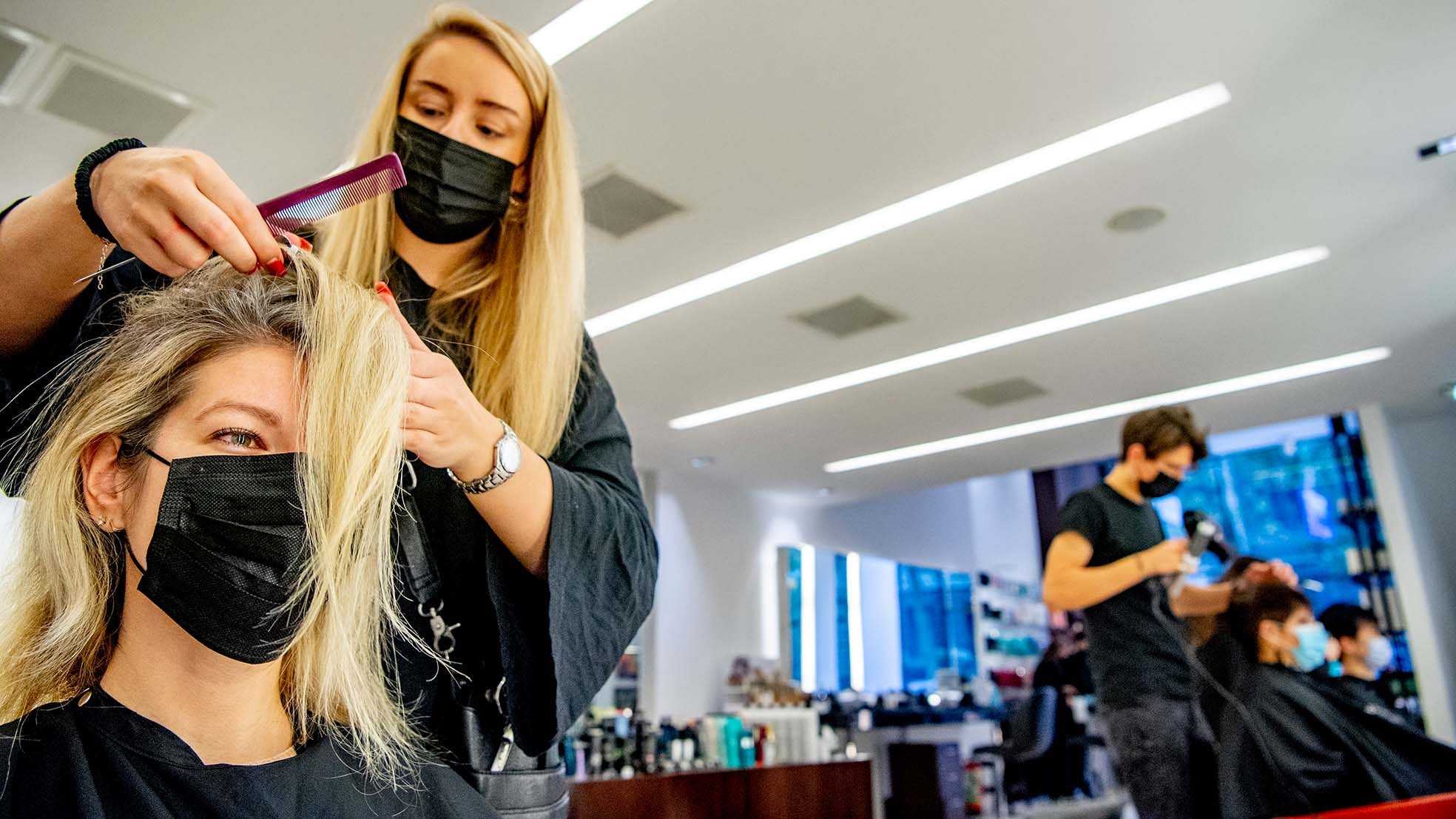 Kapster op archiefbeeld aan het werk met mondkapje op. Bron: ANP Foto