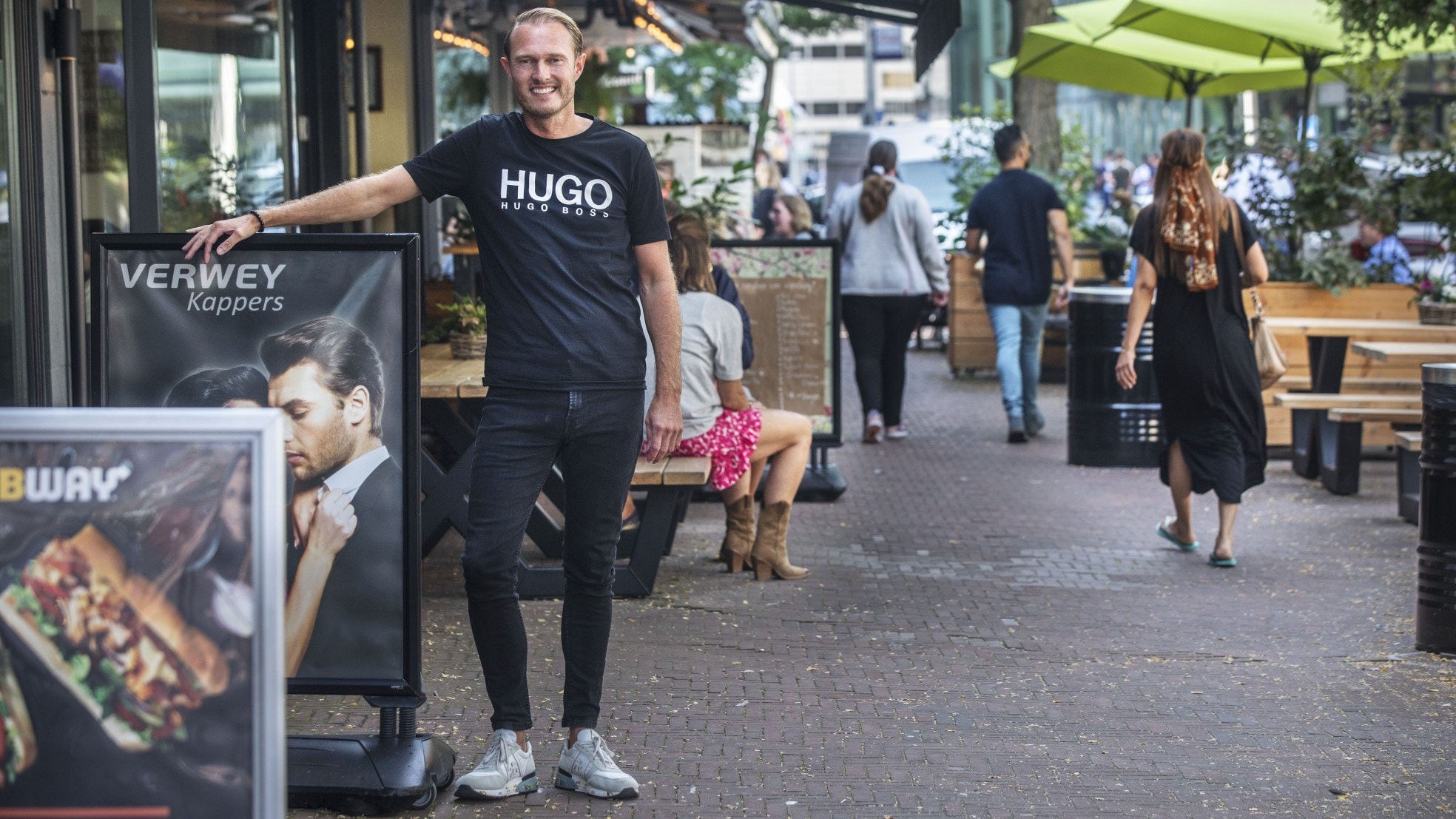 Kapper Cornell Verwey verwelkomt graag zijn nieuwe buren: ,,Ik merk deze week al dat het drukker is." Het is onbekend of de tekst op zijn shirt een speciale verwelkoming voor minister Hugo de Jonge is. Foto: Frank Jansen