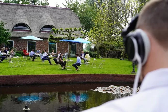 Medewerkers van Blue Bricks zitten aan First Dates-tafeltjes op het terras voor de bedrijfsboerderij van hun werkgever. Foto: Blue Bricks