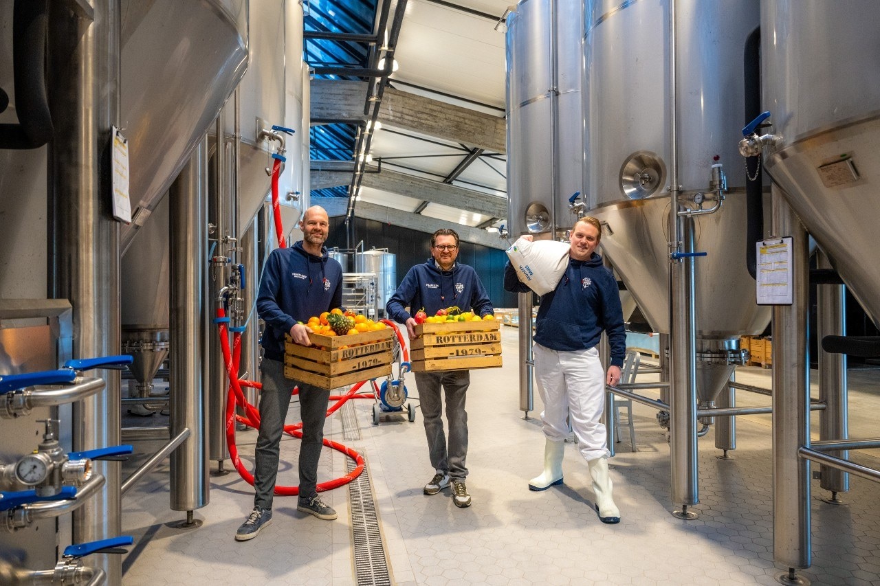 Het fruit wordt als subtiele verrijking verwerkt in een nieuwe craftbierenlijn die is geïnspireerd op de historie van de Rotterdam Fruit Port, ooit Europa’s grootste fruithaven en gelegen aan de Merwehaven. Op de foto draagt Harm van Deuren (m) een kratje fruit met rechts van hem meesterbrouwer Wesley Aarse. Foto: Arnaud Roelofsz