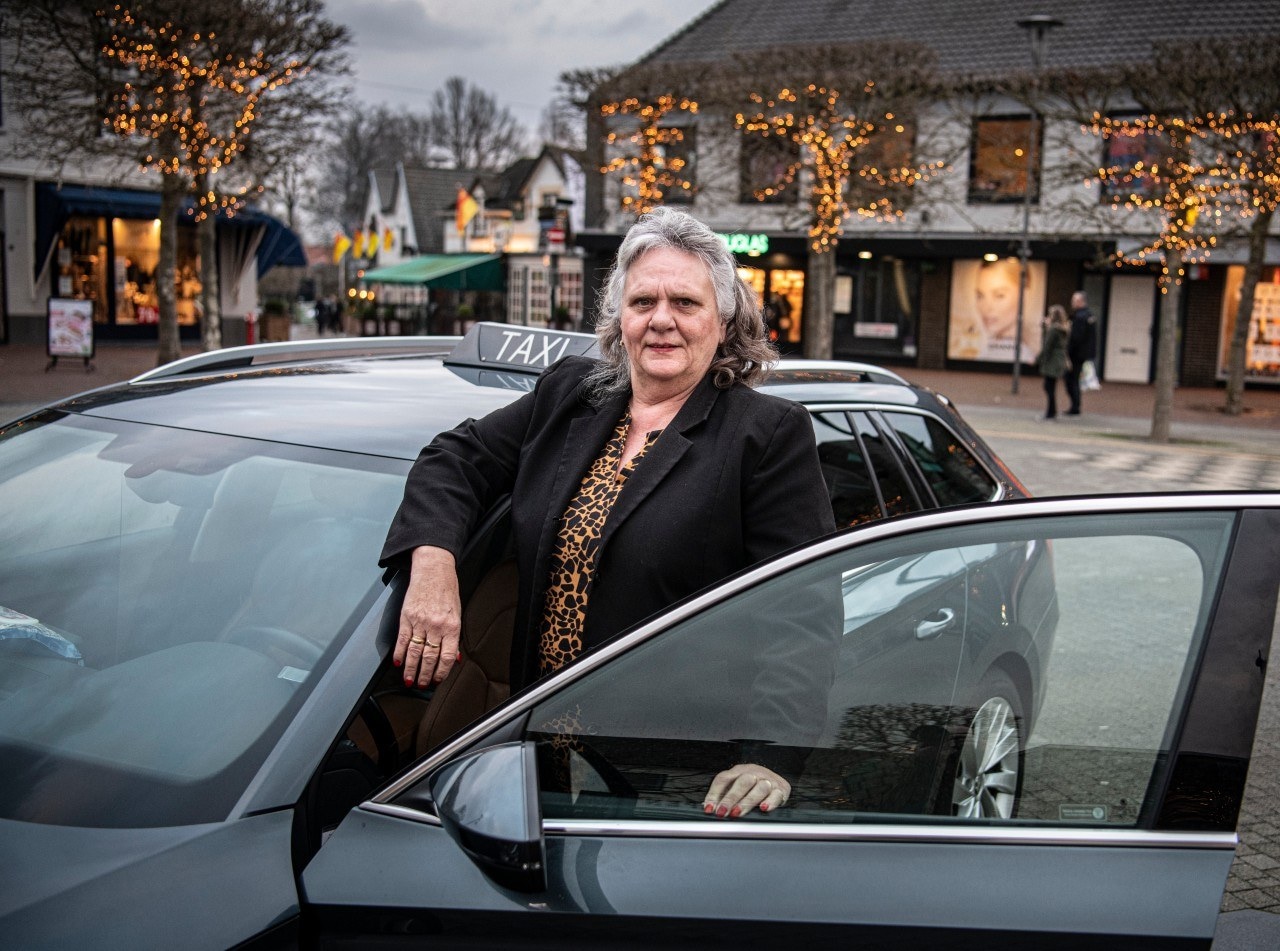 Tiny Brugman bij haar taxi. Ze had geld opzijgezet, maar de spaarrekening heeft ze afgelopen jaar bijna leeggeplunderd. Het moet. Inkomsten nul. Tiny zit thuis, te wachten tot er weer meer mag. Foto: Koen Verheijden.