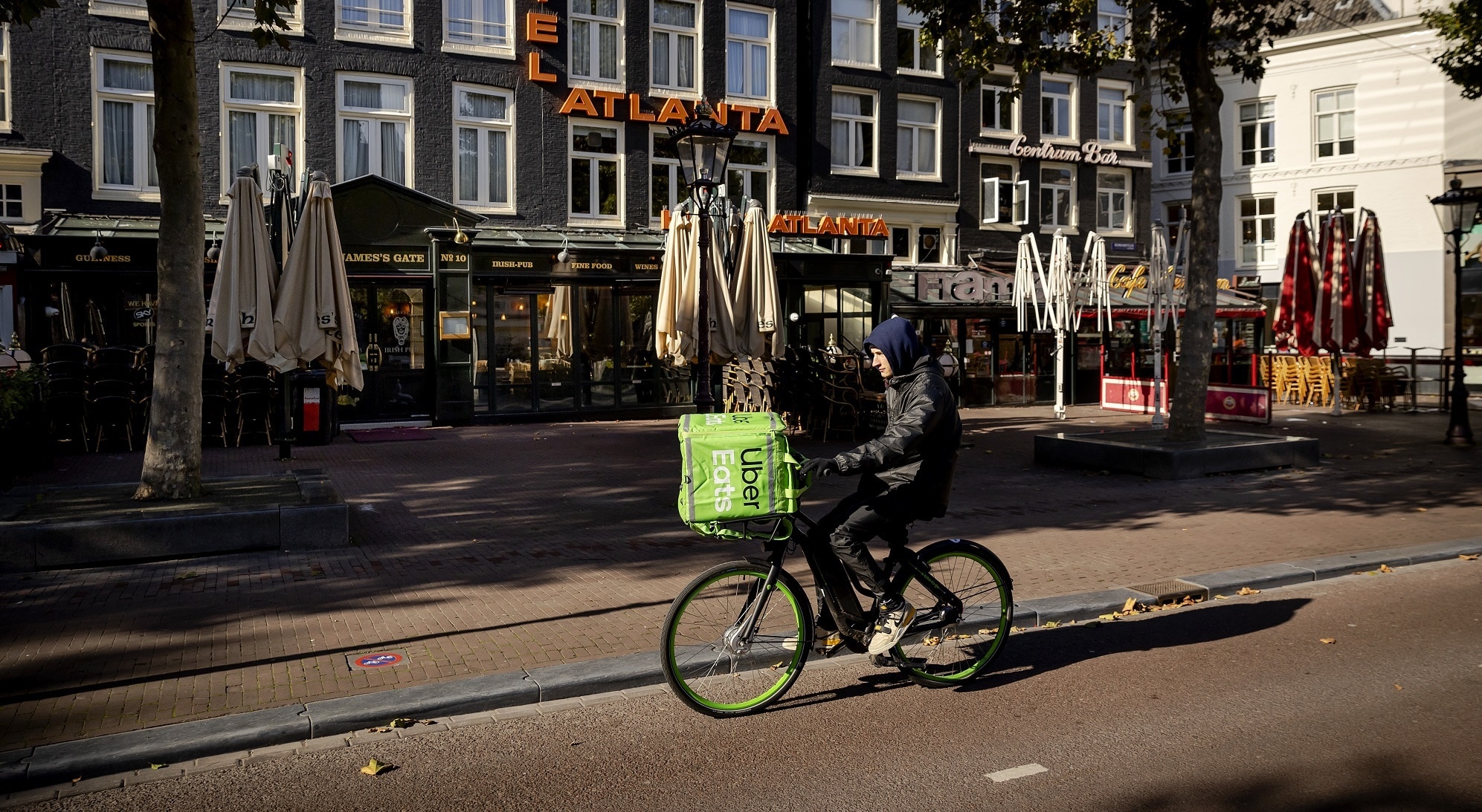 Een maaltijdbezorger fietst voorbij gesloten terrassen van horecazaken in Amsterdam. Foto: ANP