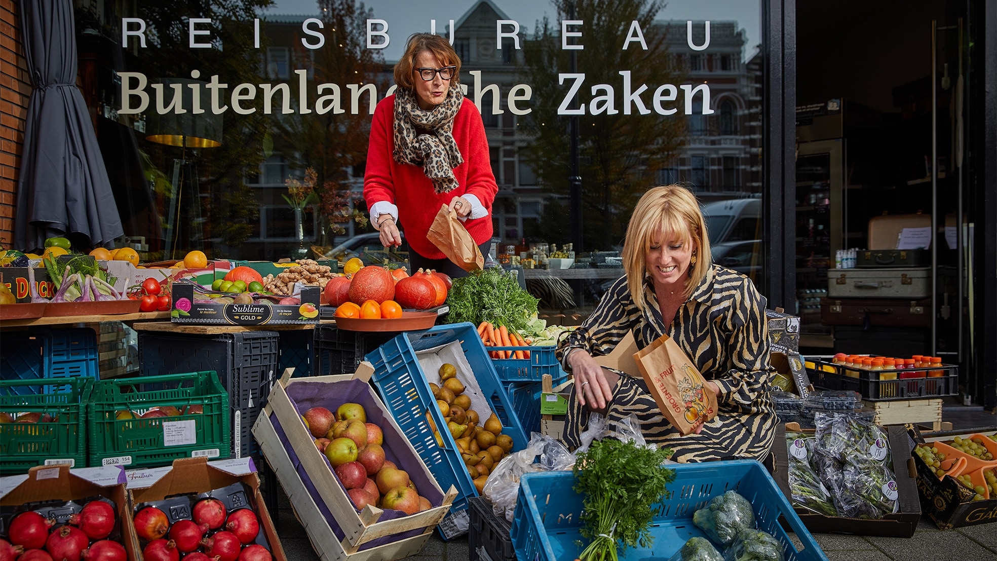 Eigenaar Joke Nuijs (links) en medewerker Lonneke van Kooten van reisbureau Buitenlandsche Zaken peuren deze coronacrisis wat inkomsten uit de verkoop van fruit, groente en vis. Foto: Jan de Groen