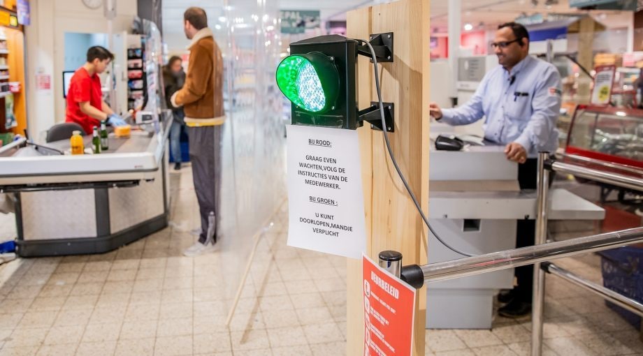 Eigenaar Nawin Harpal van supermarkt MCW Utrecht heeft een stoplicht opgehangen om te zorgen dat er niet te veel klanten in zijn winkel zijn. Foto: Shody Careman (ANP Foto)