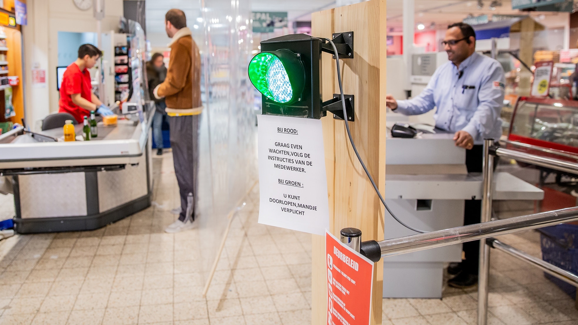 Eigenaar Nawin Harpal van supermarkt MCW Utrecht heeft een stoplicht opgehangen om te zorgen dat er niet teveel klanten in zijn winkel zijn. Om besmetting met het coronavirus te voorkomen mogen winkels een beperkt aantal klanten tegelijk toelaten. Foto: Shody Careman (ANP Foto)