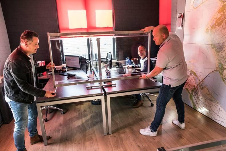 Johan Tjallinks (l) en Rick de Koning plaatsen het scheidingsscherm op het bureau van Arco Regtvoort. Foto: Arie Kievit
