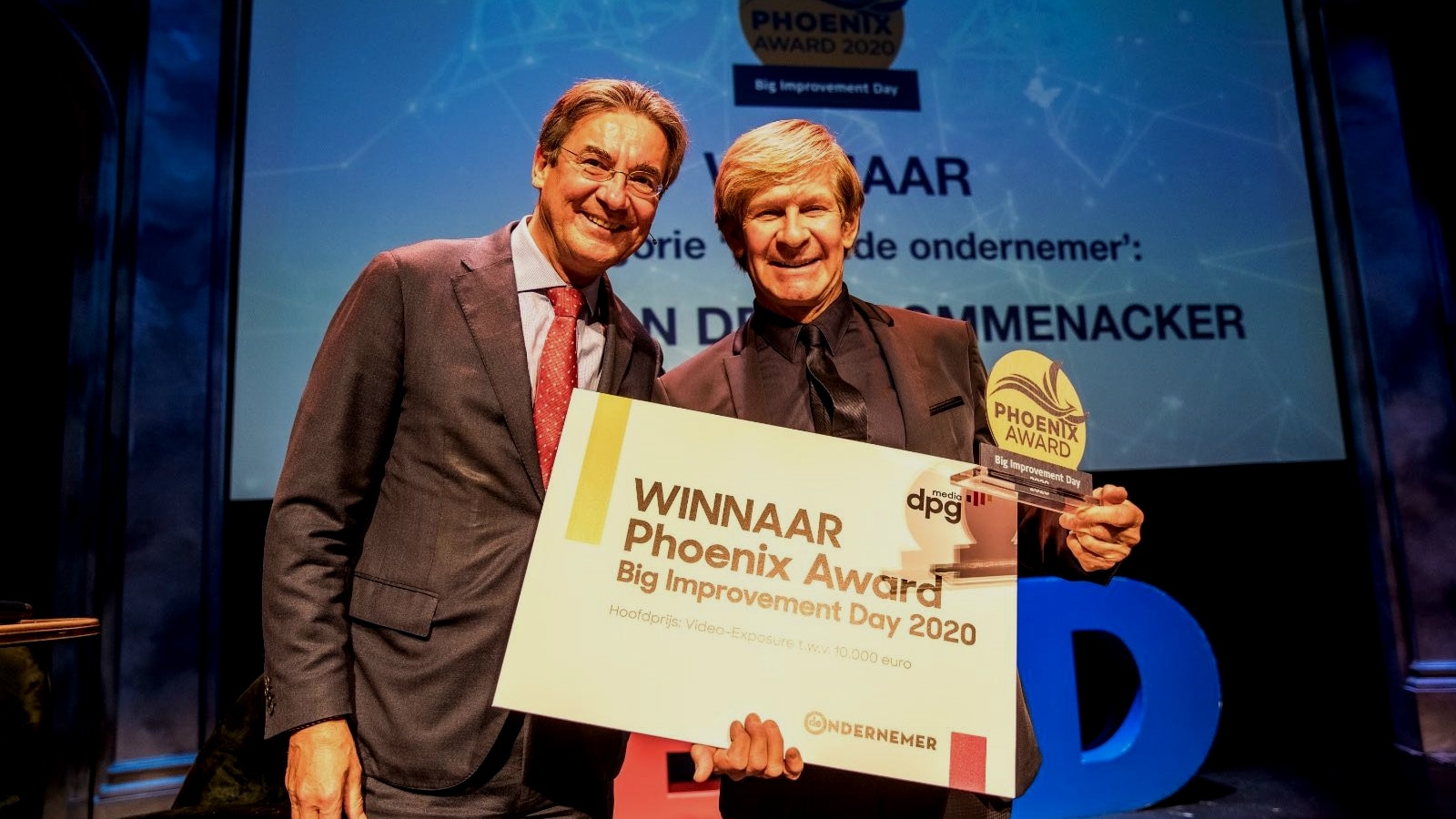 Winnaar Addy van den Krommenacker ontvangt de cheque met een mediawaarde van 10.000 euro aan videocontent uit handen van juryvoorzitter Maxime Verhagen. Foto: Jorn Baars.