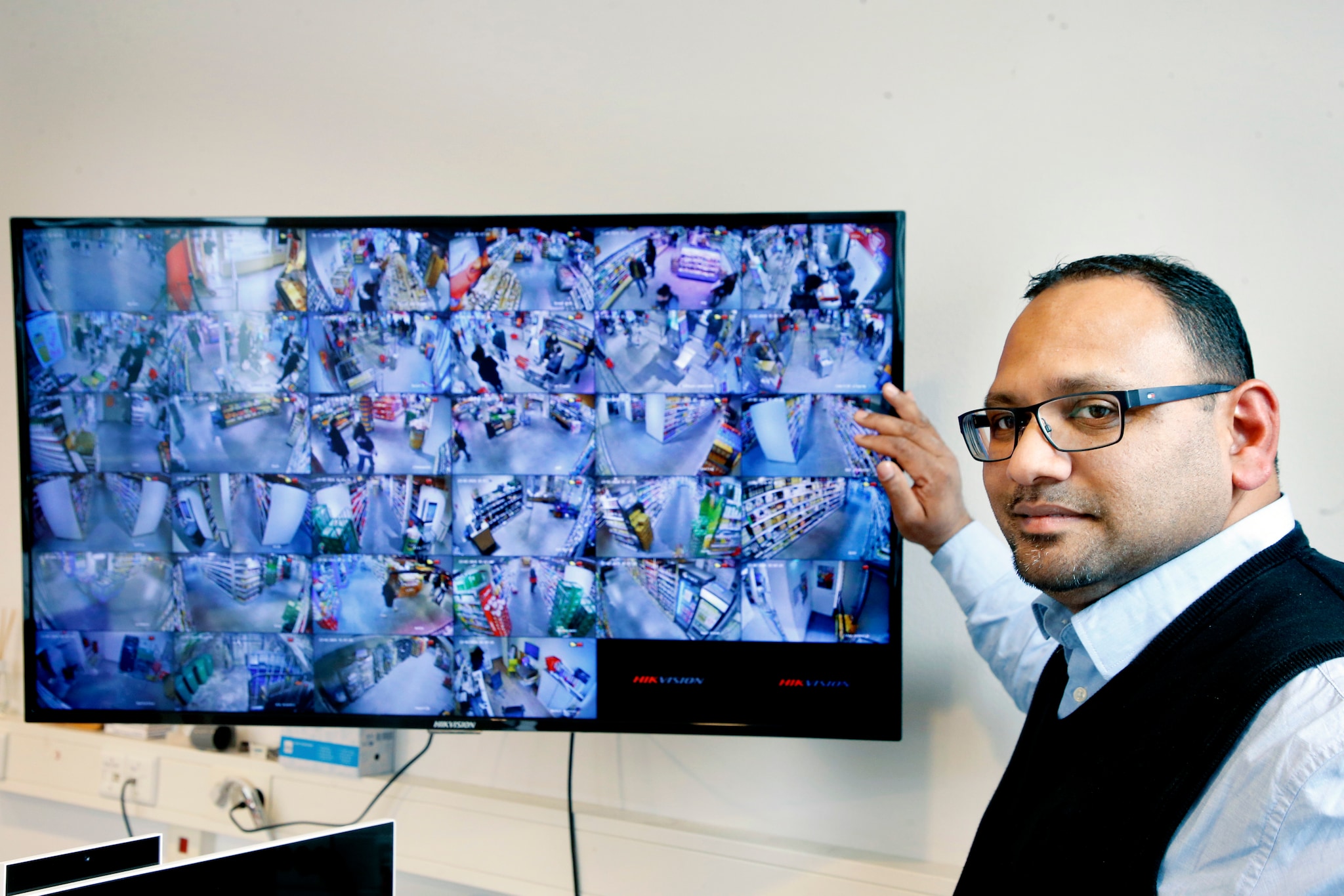 Supermarkteigenaar Nawin Harpal bij het scherm waarop alle beelden van 34 camera’s in zijn winkel te zien zijn. Ruud Voest