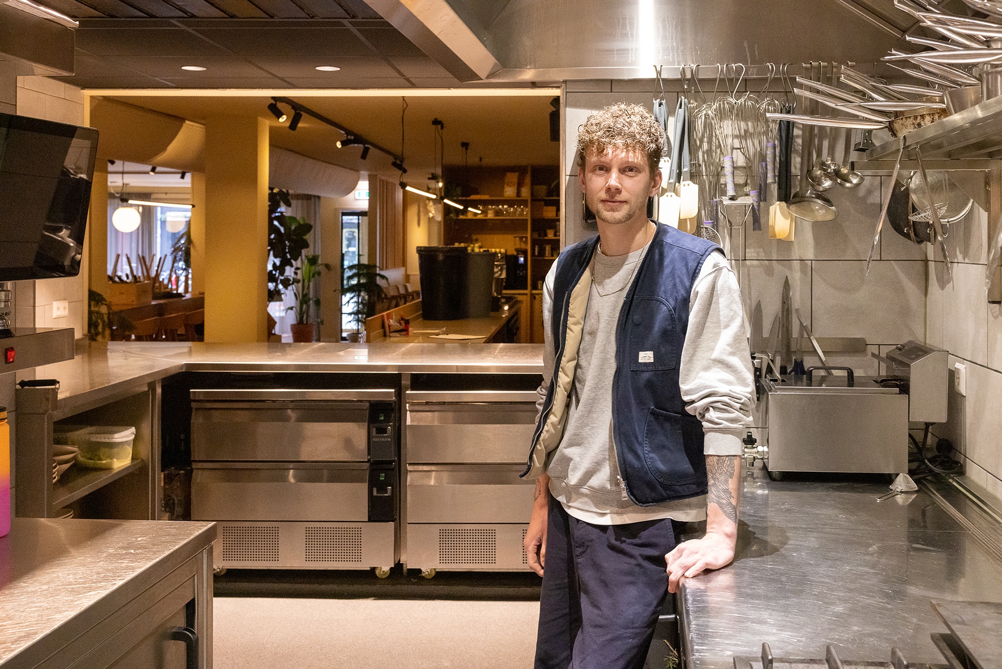 Niels van Zijl in de open keuken. Op de achtergrond is te zien hoe de stoelen op z'n kop op de tafels zijn gezet. Menno Bausch Fotografie