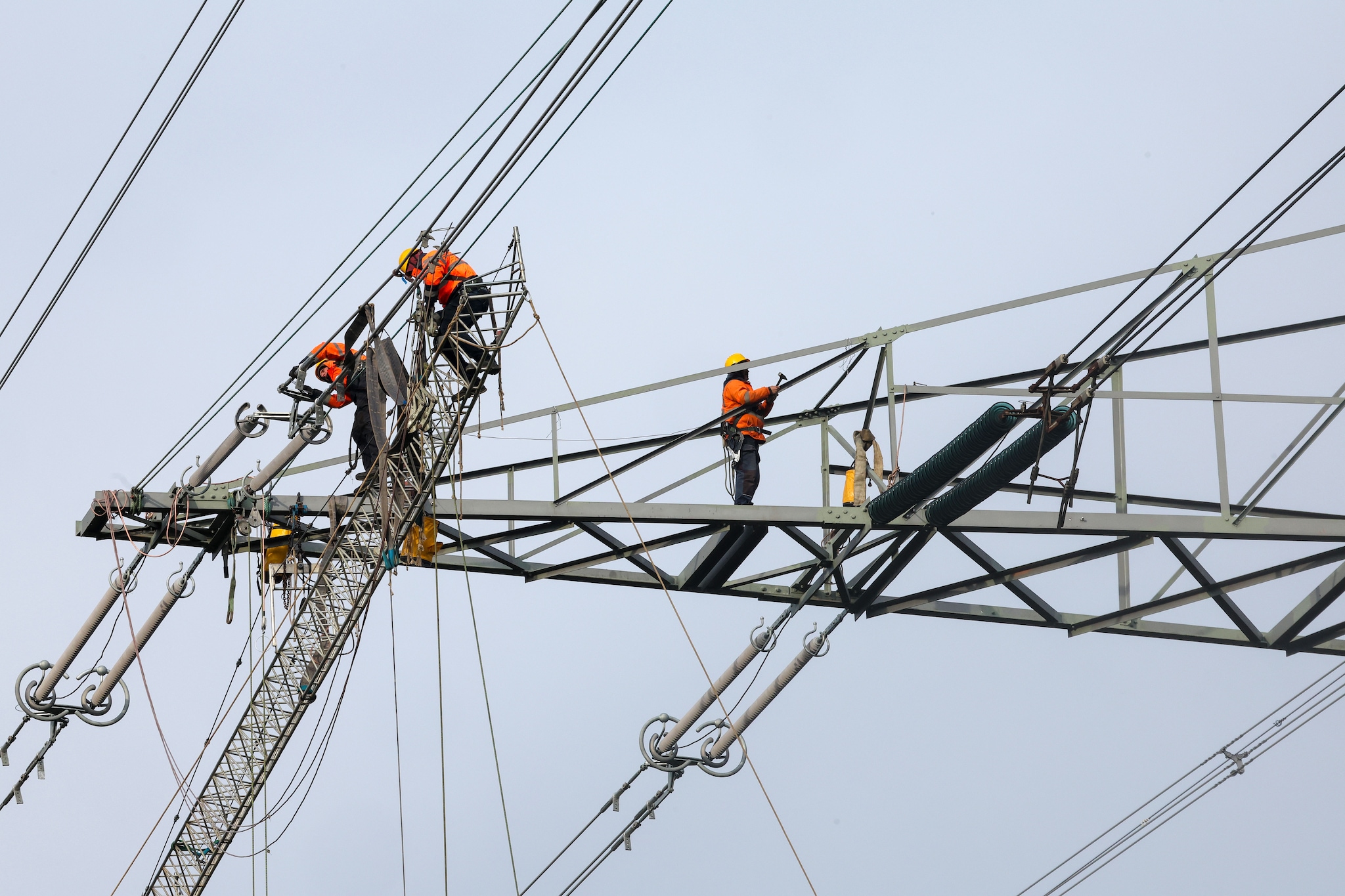 Op grote hoogte werken mannen in oranje jassen aan hoogspanningsmasten. Op grote hoogte werken mannen in oranje jassen aan hoogspanningsmasten. Foto: Bert Jansen/DCI Media