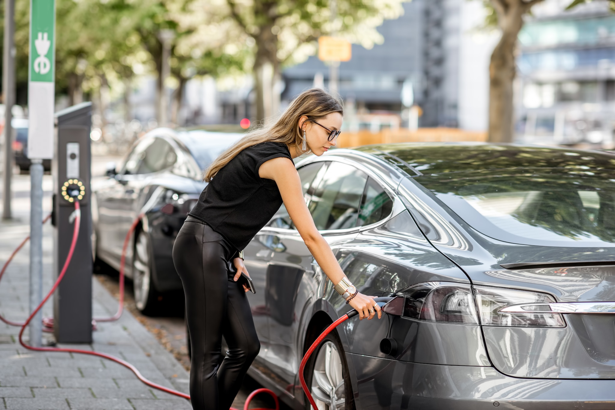 Young woman in black clothes putting connector into the electric car outdoors on the street in Rotterdam city Elektrisch rijden loont, ook voor kleine bedrijven en zzp’ers. Beeld: stock.adobe.com