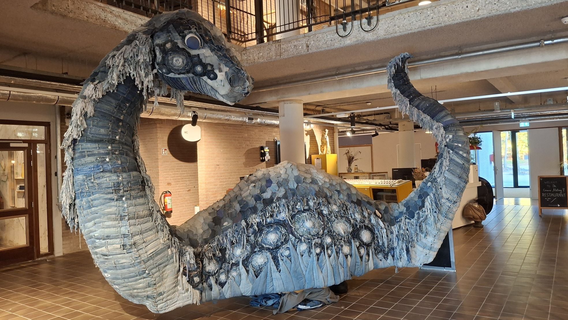 In de ontvangsthal staat een dinosaurus, gemaakt van oude spijkerbroeken.  In de ontvangsthal staat een dinosaurus, gemaakt van oude spijkerbroeken. Eigen foto